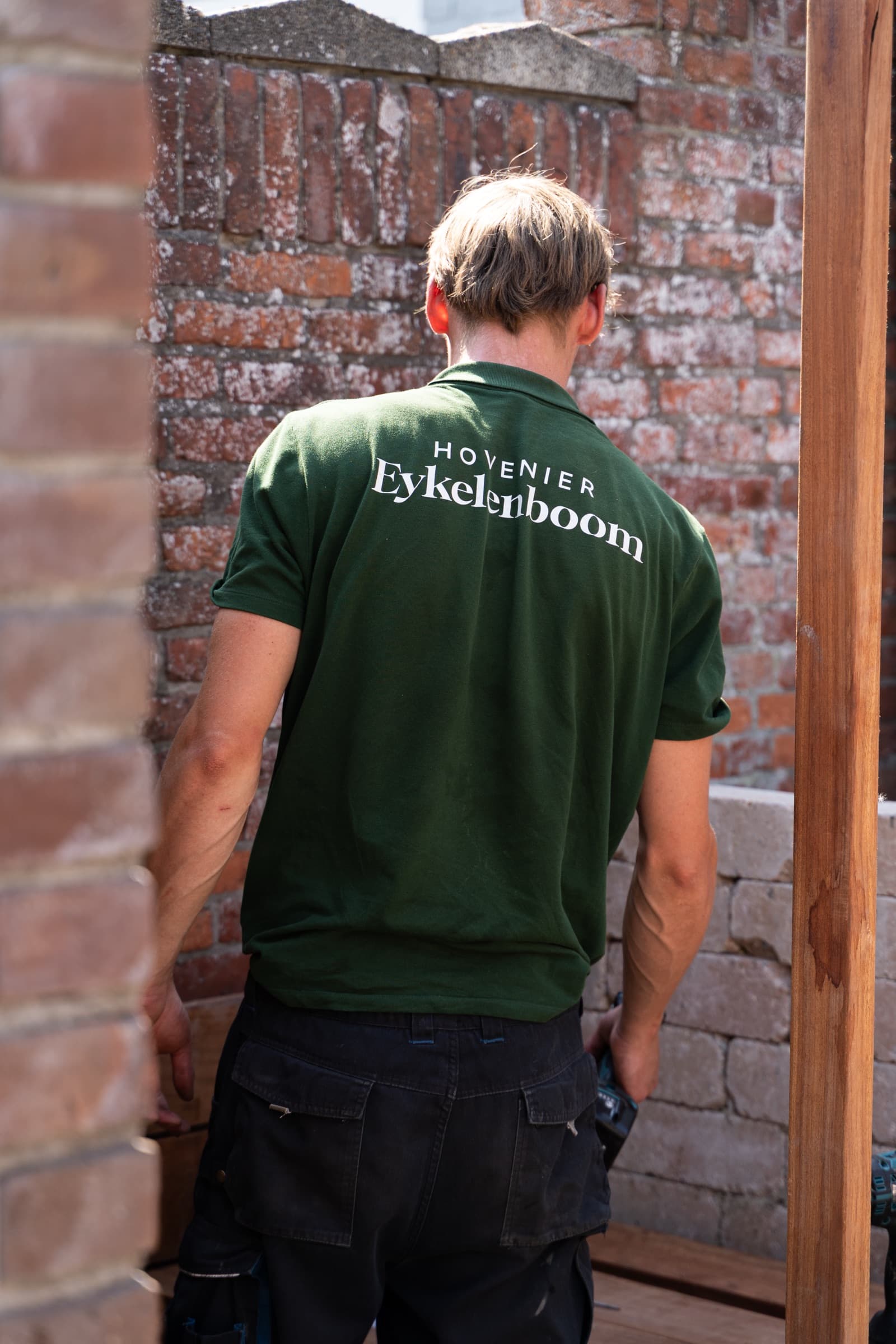 Werkpolo met het logo van Hovenier Eykelenboom op de rug, tijdens het werk in de tuin